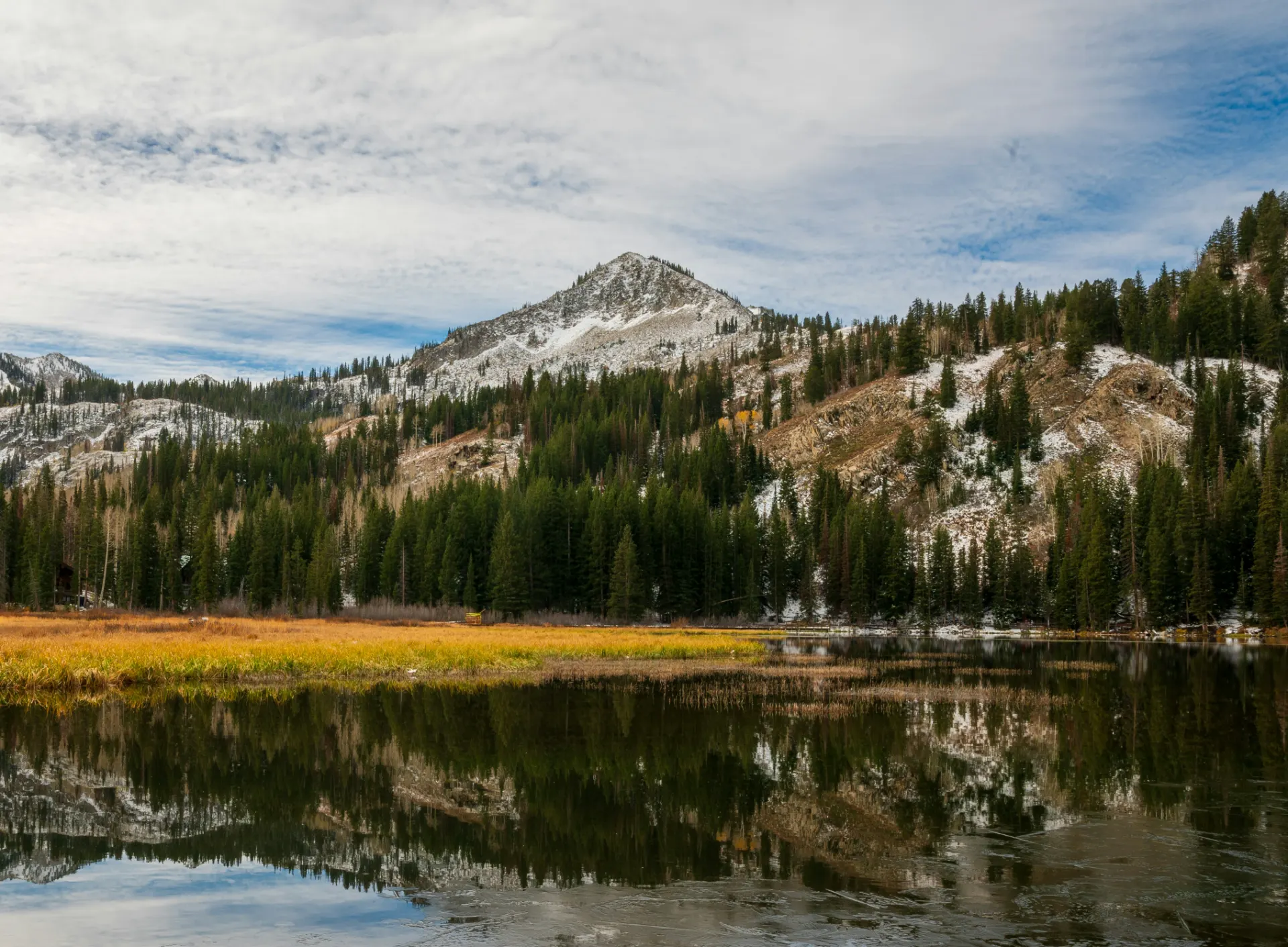 A snow-dusted Wasatch peak and conifers reflected in a still alpine lake
